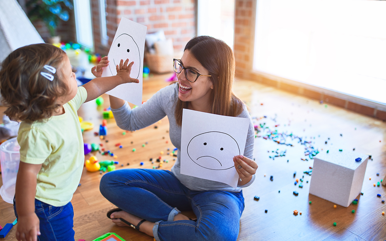 Teacher with toddler learning to communicate emotions with drawing of smile face and frown face